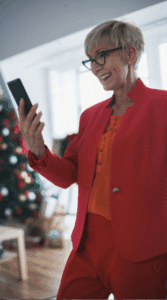 mature woman with short hair, a red suite and glasses recording a video with her smartphone